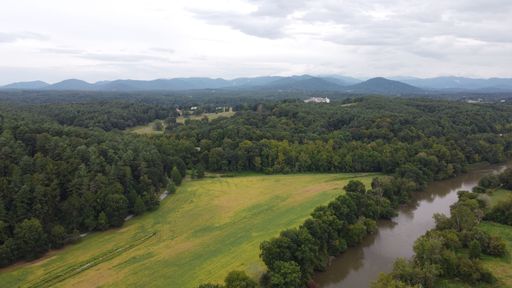 An aerial shot of countryside with green field surrounded by lush dense forests next to narrow river
