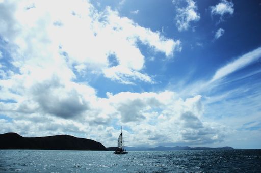 A sailboat sailing on blue water under a bright cloudy sky