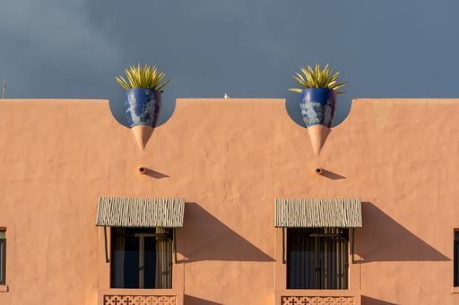 A low angle shot of the exterior design of an orange building with two plan pots on the top