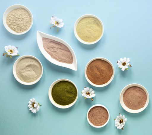 A selection of ceramic bowls with colorful powders and flowers on a blue background