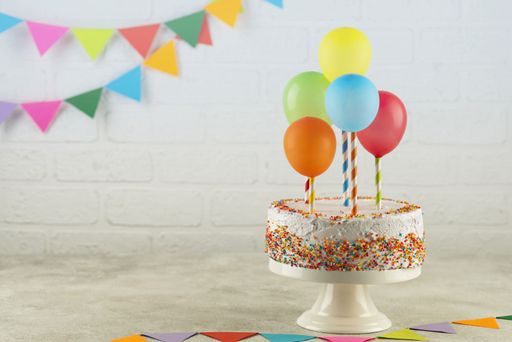 A birthday cake with balloons and sprinkles on a white background