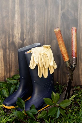 A pair of rubber gardening boots and gloves on a wooden background