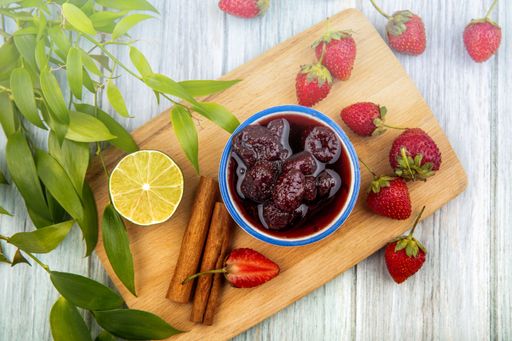 A bowl of fresh strawberry jam with lime slices, cinnamon sticks, and mint leaves on a cutting board