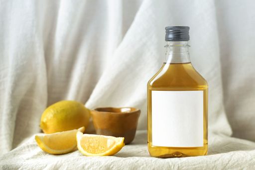 A clear glass bottle of orange juice on a light wooden table, next to lemon slices