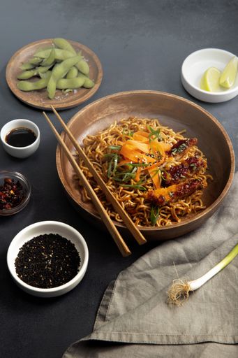 A dining table with a steaming bowl of noodles and vegetables