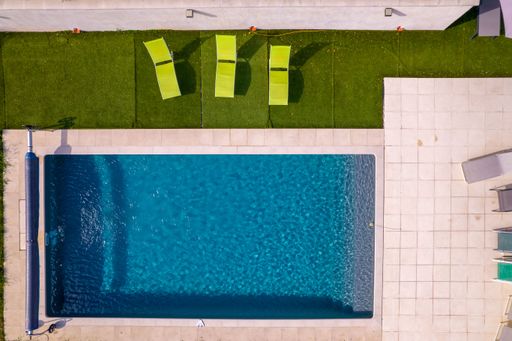 An aerial view of a swimming pool surrounded by synthetic grass and three green deck chairs