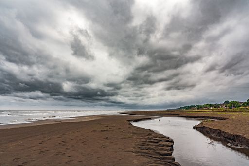 A tranquil beach scene featuring a large puddle of water near the edge of the ocean and a cloudy sky in the background