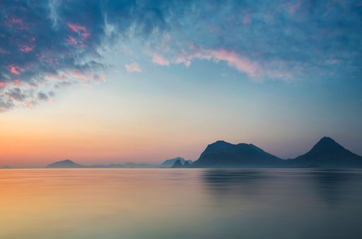 A beautiful scenery of sea under cloudy sky with cliff in the background at sunset