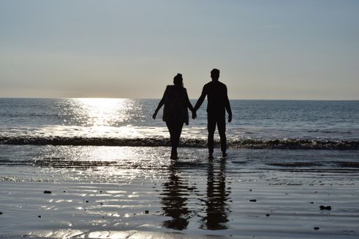 A majestic shot of a silhouette of a young couple walking barefoot on sandy coastline