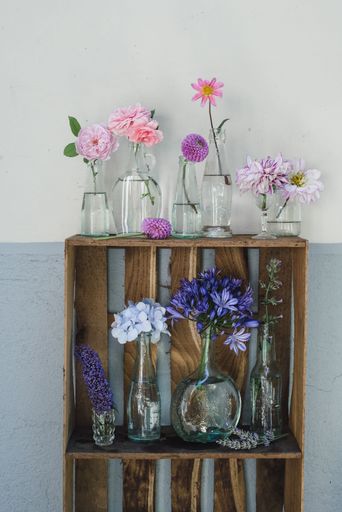 A vertical shot of assorted colorful flowers in individual vases on a two-layer wooden shelf