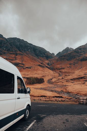 a vertical shot of a white van parked near scottish highlands