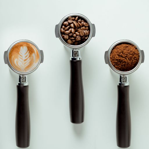 Top view of barista coffee machine scoops filled with coffee beans, powder and cappuccino on white surface