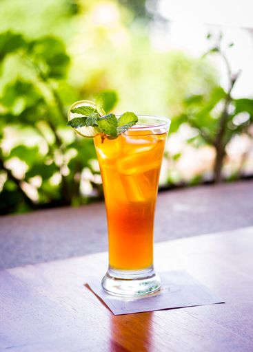 A vertical shot of an ice tea, with lemon slice and mint on wooden table on blurry garden background