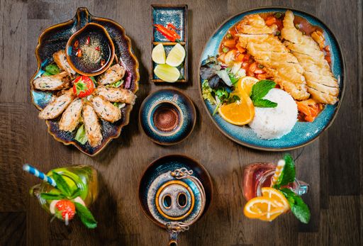 A top view of a table with gourmet Asian dishes like bun cha, fried chicken and iced lemonade