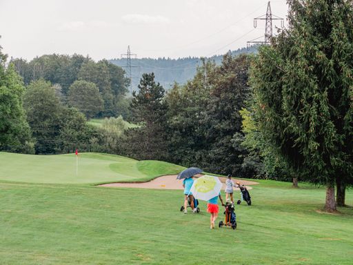 Two female friends strolling leisurely on a golf course, both protected from the rain beneath matching umbrellas