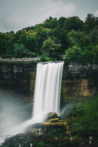 A vertical mesmerizing view of a gracefully falling waterfall on cliffs in the forests