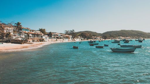 A horizontal aerial shot of a Rio de Janeiro beach with houses on it and many boats in the sea