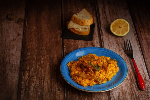 blue colored rice plate with ribs, lemon and bread on a wooden table with cutlery
