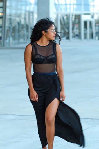 A vertical shot of a curly brunette Hispanic female posing in a beautiful transparent black dress