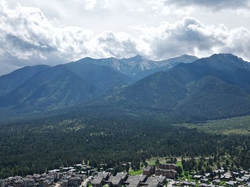 An aerial shot of a small town surrounded by mountains and green trees on a summer day
