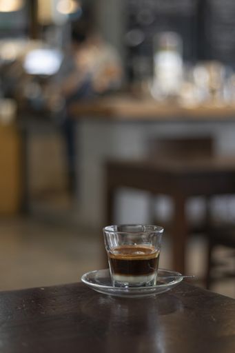 A vertical selective focus shot of a small cup of espresso with a plate on a cafe table