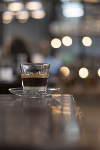 A vertical selective focus shot of a small cup of espresso with a plate on a cafe table