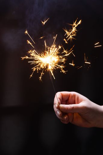 A vertical shot of a hand holding a burning sparkler on a dark background
