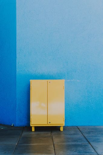 A vertical shot of a bright yellow metallic cabinet placed against a blue wall