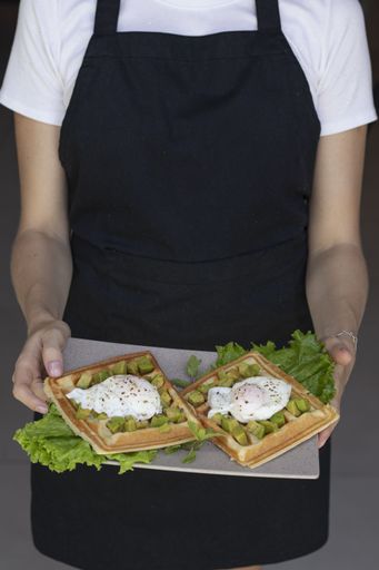 A vertical shot of a chef holding a plate of gourmet waffles with poached eggs and avocadoes
