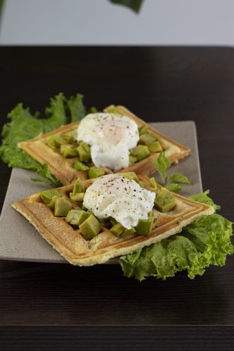A vertical shot of waffles with avocado and poached eggs