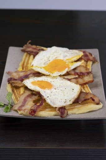 A vertical shot of a gourmet breakfast with waffles, eggs, and bacon