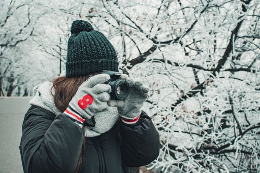 Unidentified girl taking photos in the snow with a hood and gloves with a red B on it. Trees on the background. Canon 750D.