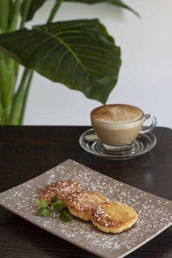 A vertical shot of a plate of traditional syrniki and a cup of cappuccino on a table