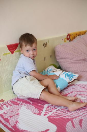 A Caucasian cute boy kid playing with pillows on bed at home