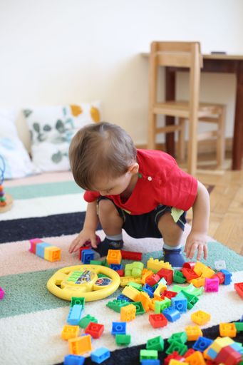 A Caucasian boy kid sitting and assembling colorful cubes at a Kindergarten, vertical shot