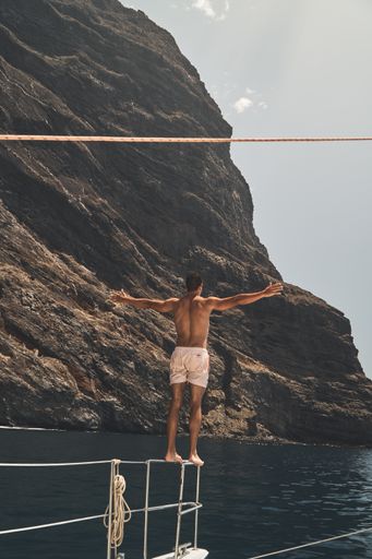 A vertical shot of a man standing on boat railings with arms widespread and looking out into the sea - concept of freedom