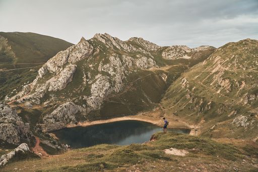 A male backpacker looking at the lake at Somiedo Natural Park in Asturias Spain, on a cloudy day