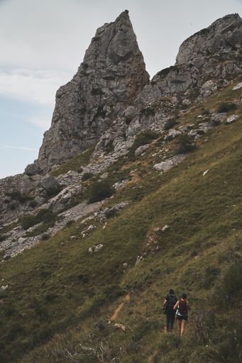 A vertical shot of a hiker couple hiking on a mountain with rocky peaks at the Somiedo Natural Park in Spain