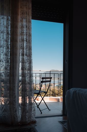 A vertical shot of a balcony or veranda with a chair and a picturesque view of the seaside