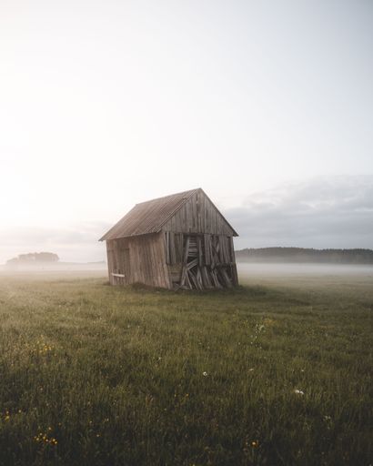 A vertical shot of a damaged wooden hut in the meadow