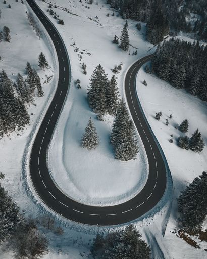 A vertical aerial shot of a curvy road through the spruce trees in winter