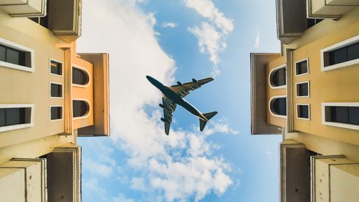 An aircraft flying over buildings under a cloudy blue sky
