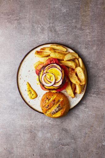 A vertical top view of an open gourmet burger with fries