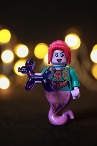 A toy female genie figure with red hair and lips holding a purple balloon animal