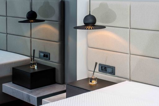 A high angle shot of two beds, two incents on neat bedsides and two lamps hung above them
