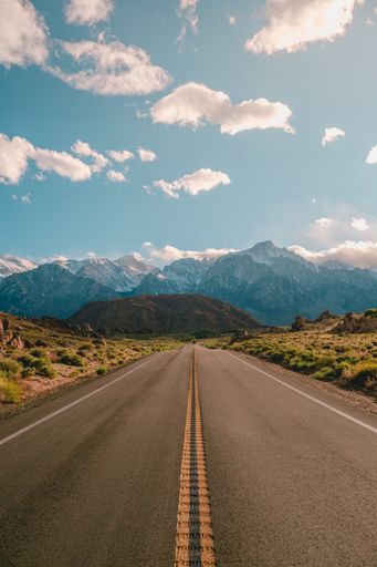 A vertical shot of a road with the magnificent mountains under the blue sky captured in California