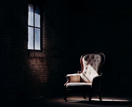 A beautiful shot of a retro chair in the dark empty room with a strip of window light falling on it