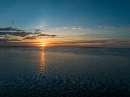 A lovely aerial view of a golden sun shining brightly down on a dark blue sea before sunset