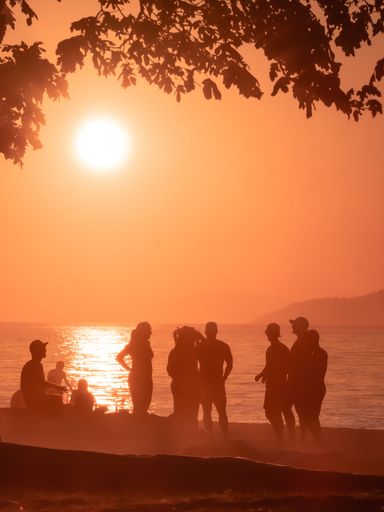 A vertical shot of people near the sea at sunset in Vancouver, Canada