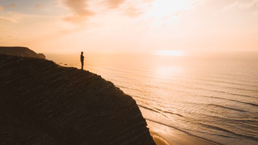A beautiful view of a person standing on a cliff over the ocean at sunset in Algarve, Portugal